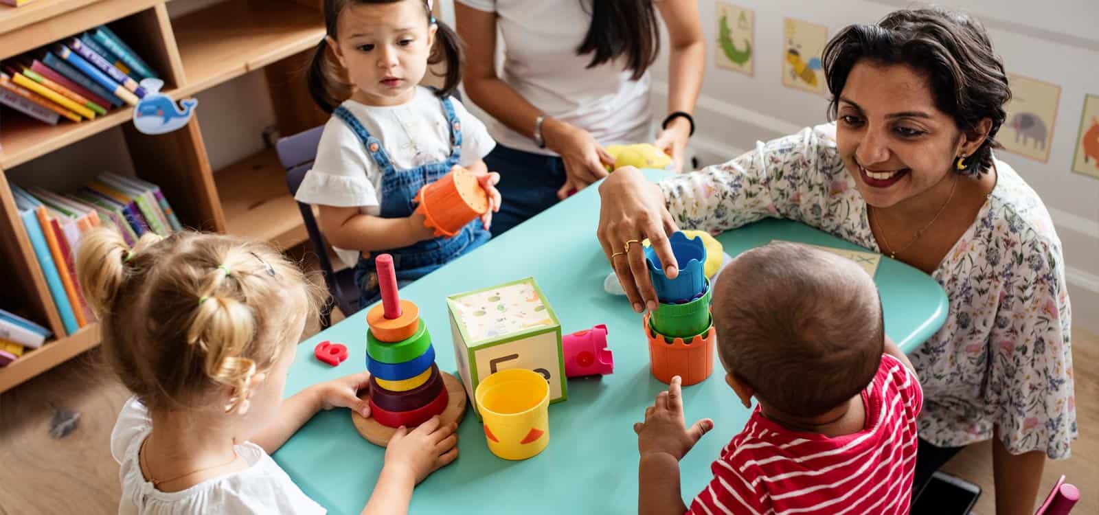 A woman is surrounded by children and plays with toys with them, indicating she pursued the business idea of becoming a daycare owner