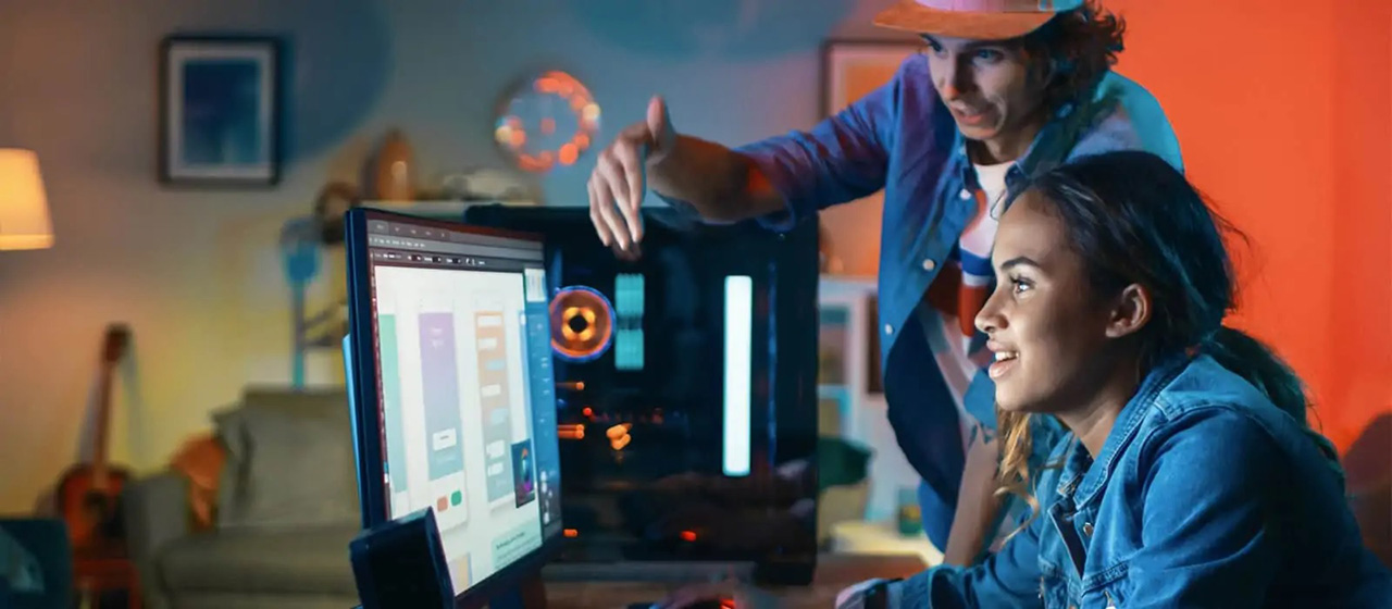 One female and one male staring into the same monitor in a room with multicolored lights