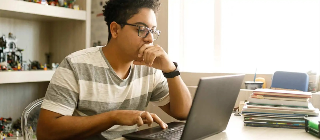 Male in striped shirt scrolling on black laptop 