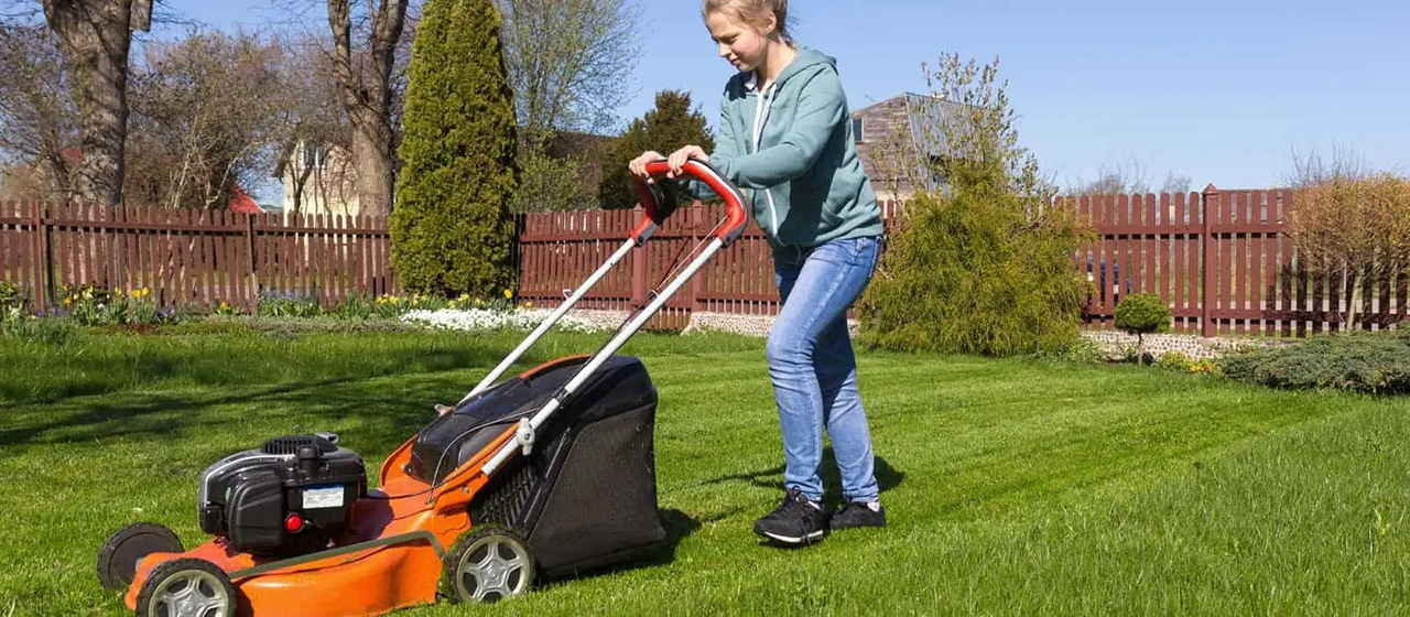 Female steering an orange lawnmower on a lawn in a backyard