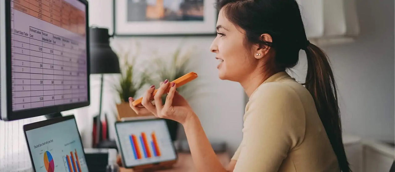 Woman on phone while looking at spreadsheets on computer