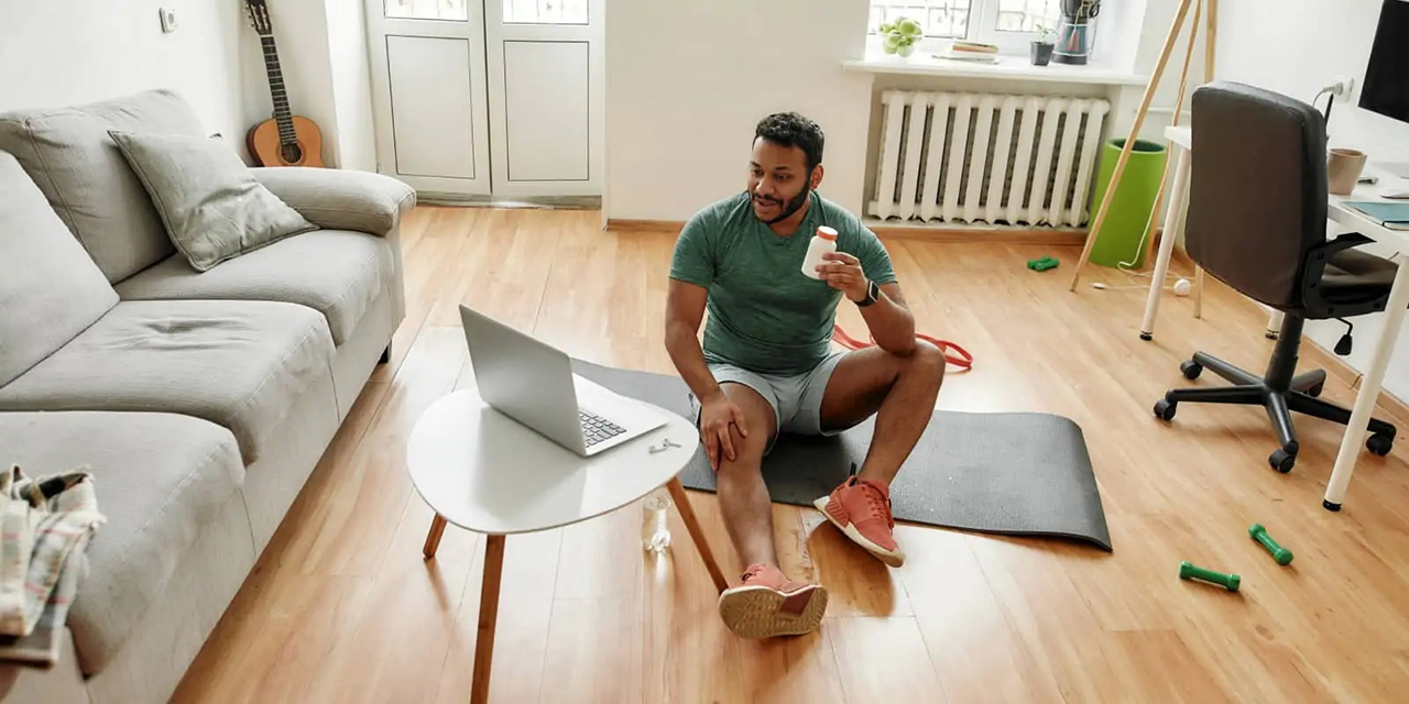 Man on wood floor with yoga mat doing a workout over video call on laptop