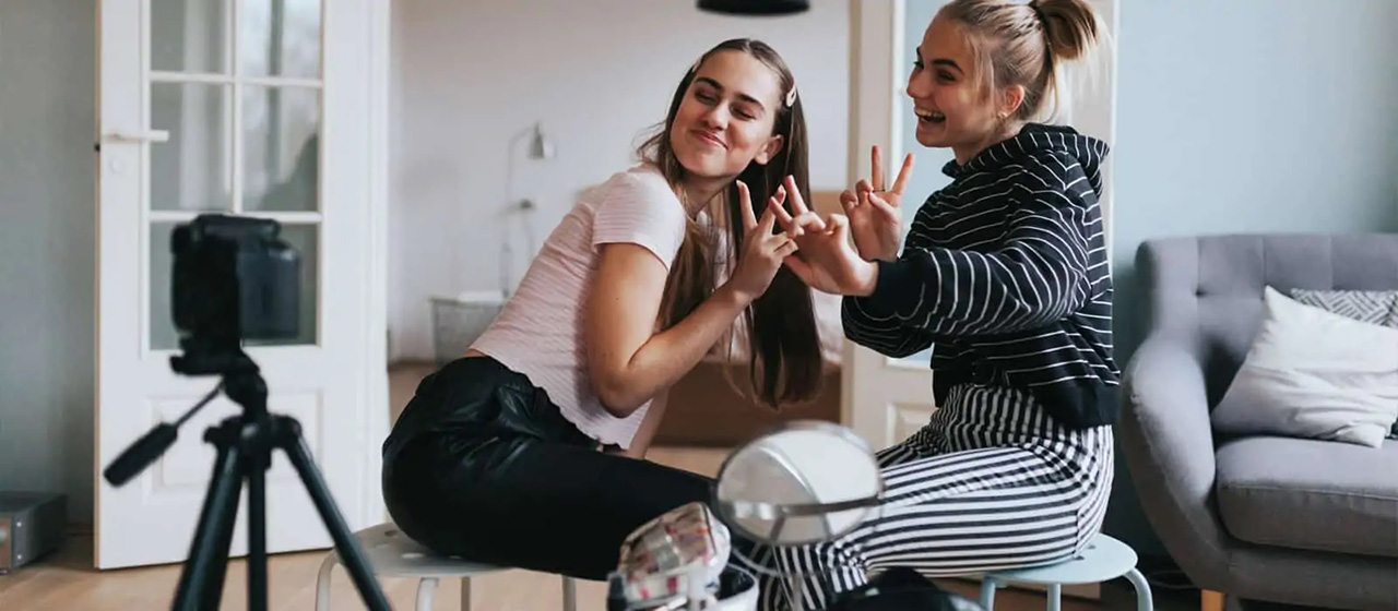 Two girls posing with peace-signs in front of a camera on a tripod