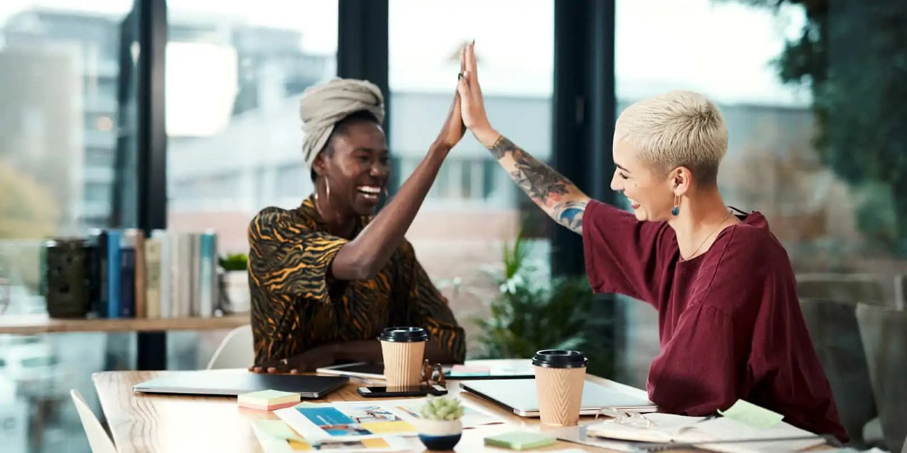 Two women high fiving next to coffee cups and paper on a table