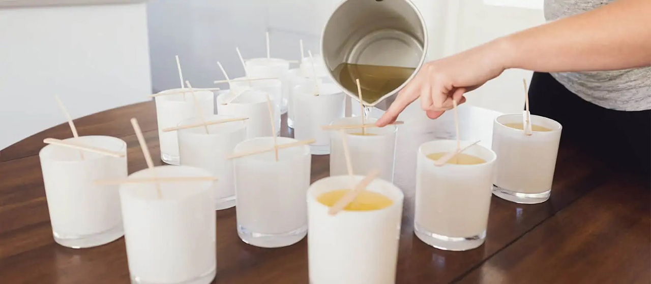 Candle maker pouring wax into multiple candles from a pot