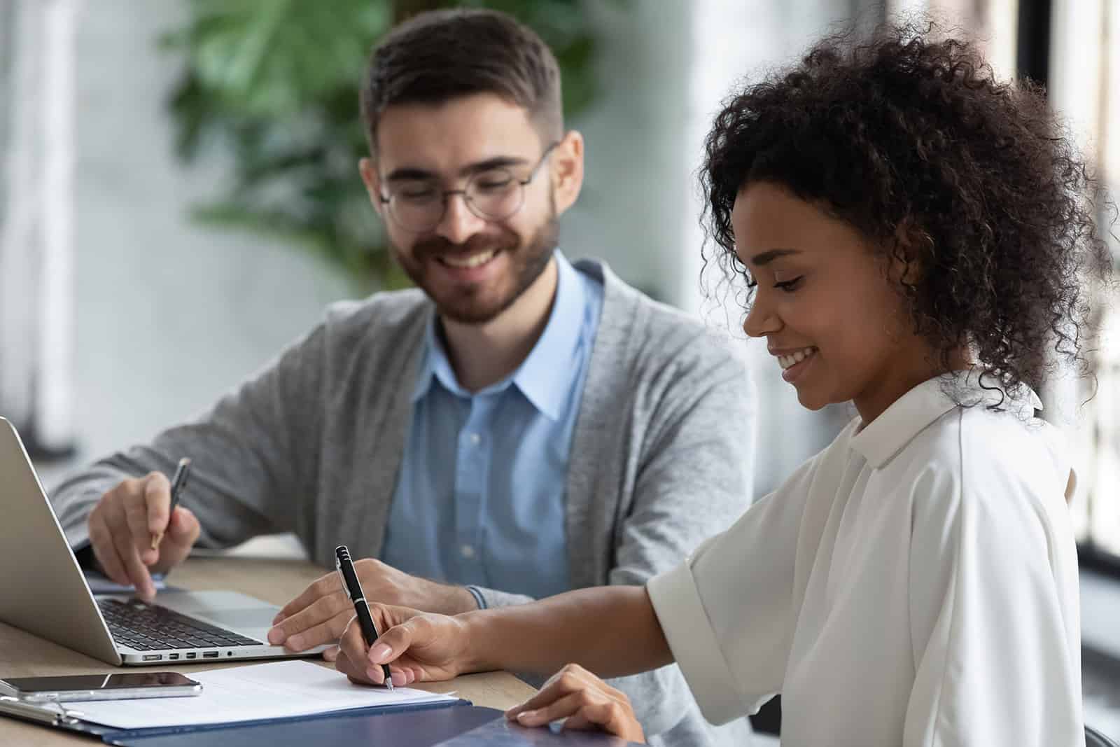 Man and woman signing paperwork and smiling in front of laptop